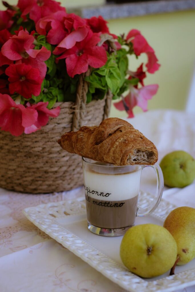 bitten croissant lying on coffee glass near pears and flowers